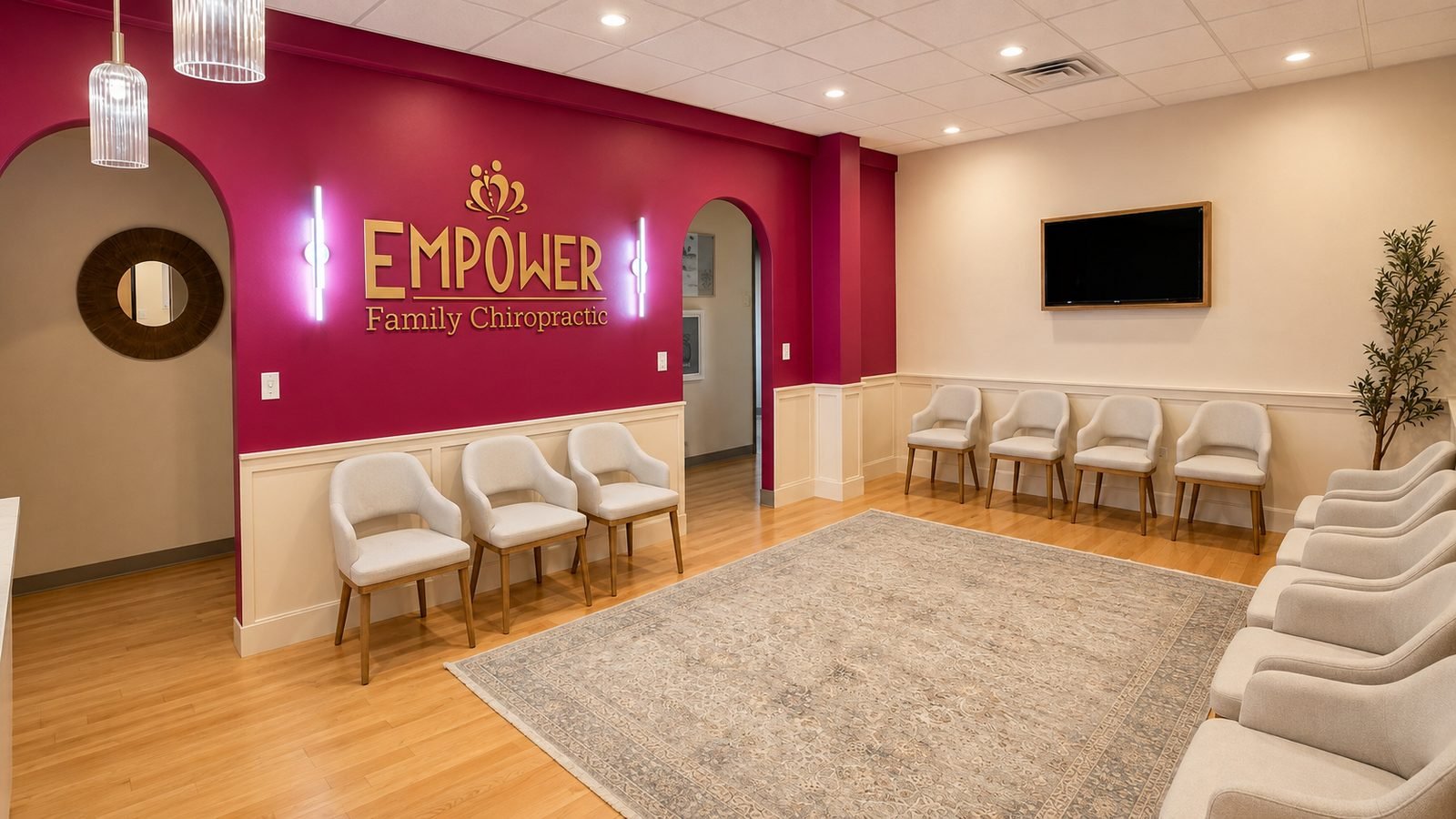 Reception area at Empower Family Chiropractic in Lakeway with the practice's gold logo on a magenta wall, upholstered chairs, and a large area rug