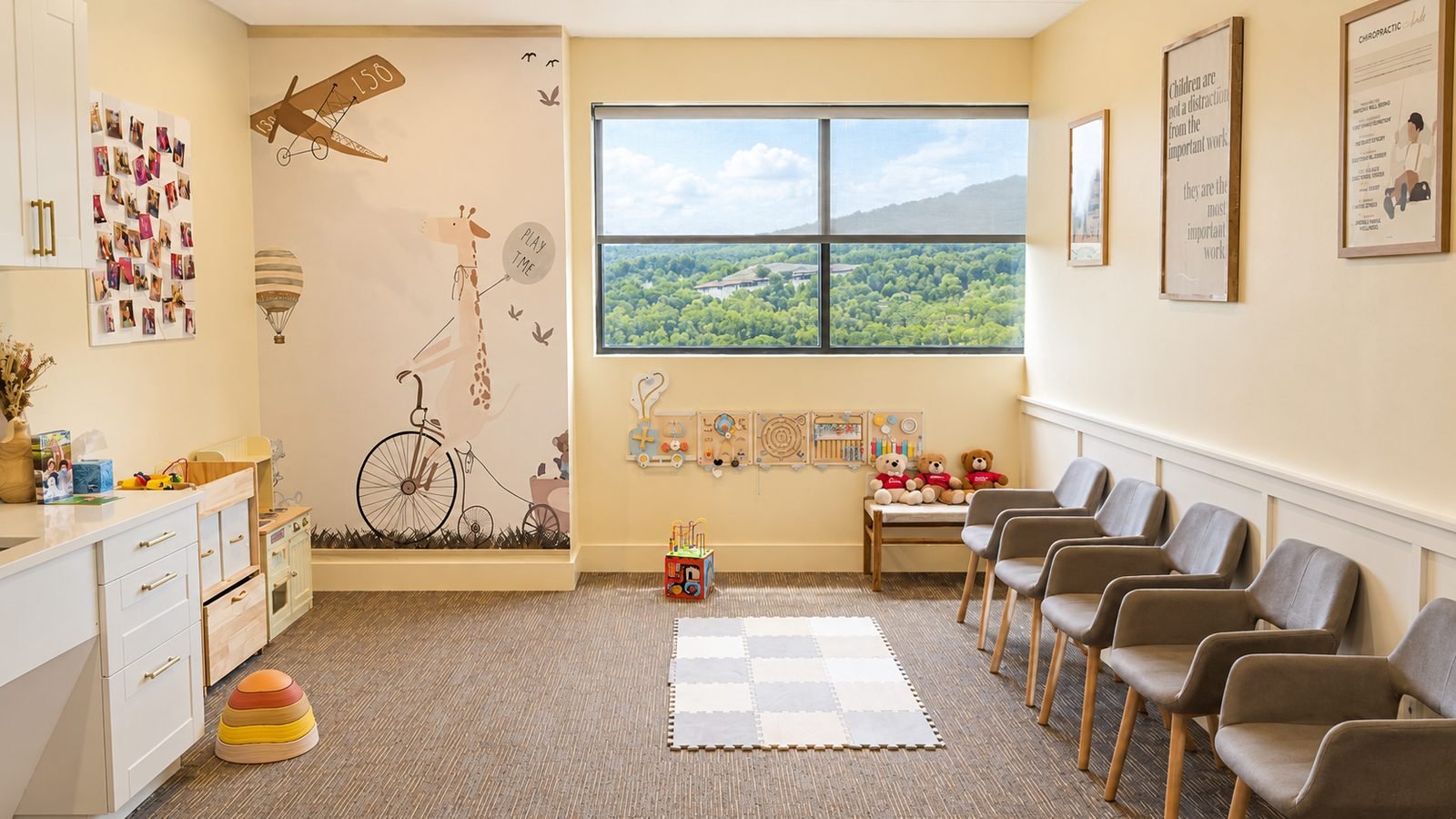 Children's play area at Empower Family Chiropractic in Lakeway, Texas, with a giraffe wall mural, wooden activity boards, a foam play mat, and a window view of the Hill Country